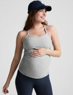 Woman wearing a gray maternity tank top and navy cap on a light gray background.