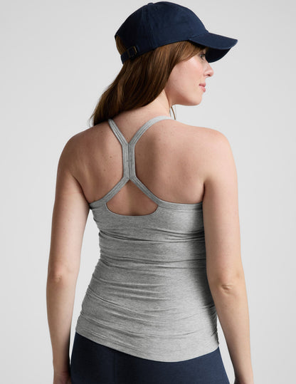 Woman wearing a gray maternity tank top and navy cap on a light gray background.