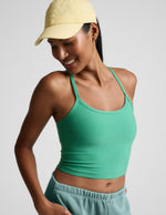Woman wearing a green cropped tank and light blue shorts with a yellow cap on a plain background.