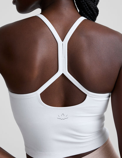 woman wearing a white racerback cropped tank and pink pants against a plain background.