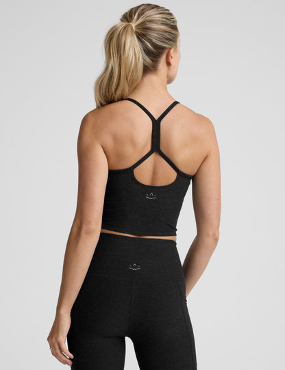 woman wearing a black racerback cropped tank and leggings on a plain background.