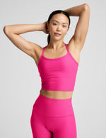 Woman wearing a bright pink cropped tank and leggings on a light gray background.