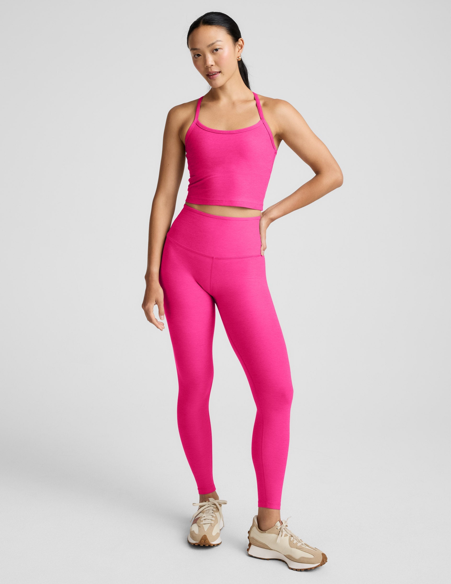 Woman wearing a bright pink cropped tank and leggings on a light gray background.