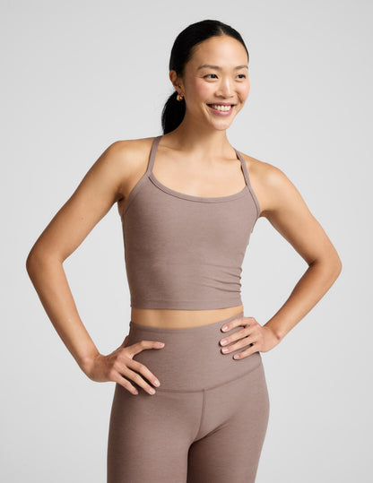 Woman in a brown tank top and leggings against a plain background.