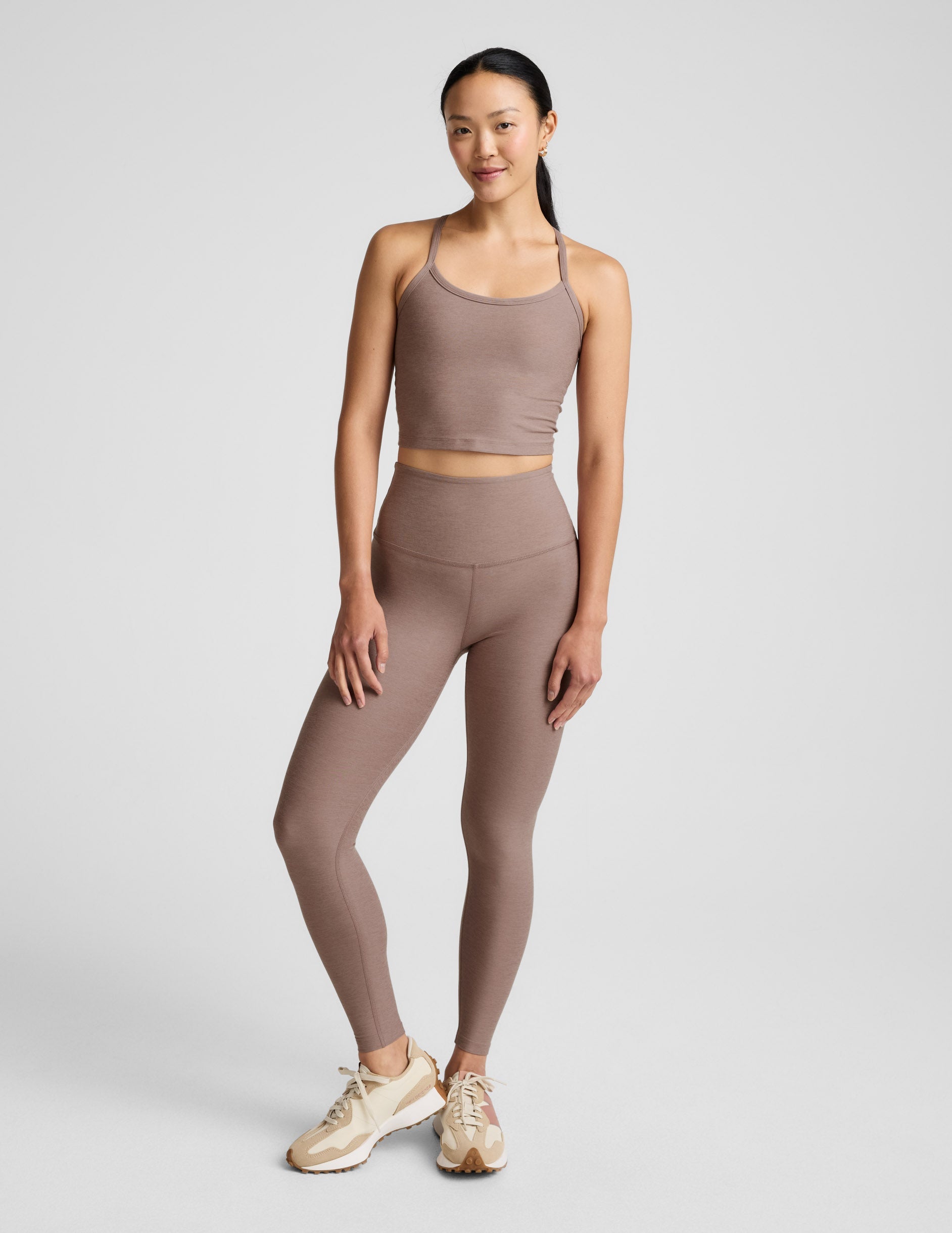 Woman in a brown tank top and leggings against a plain background.