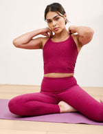 Woman in pink athletic wear sitting on a yoga mat with a white background.