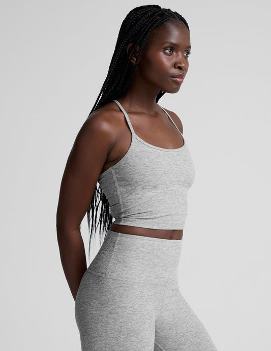 woman is wearing a gray racerback cropped tank and gray leggings against a plain background.