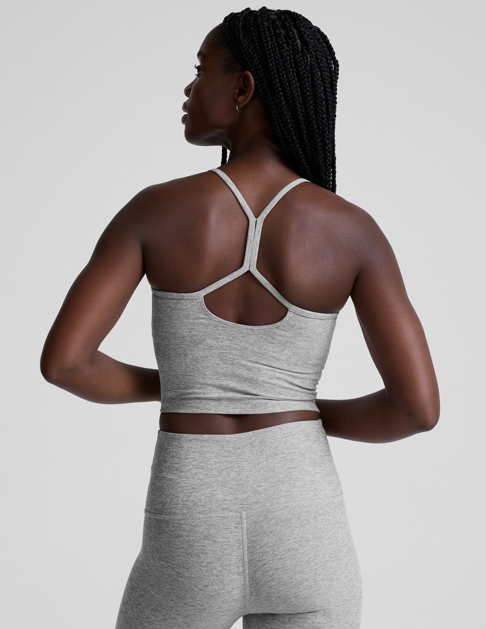 woman is wearing a gray racerback cropped tank and gray leggings against a plain background.