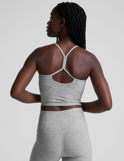 woman is wearing a gray racerback cropped tank and gray leggings against a plain background.