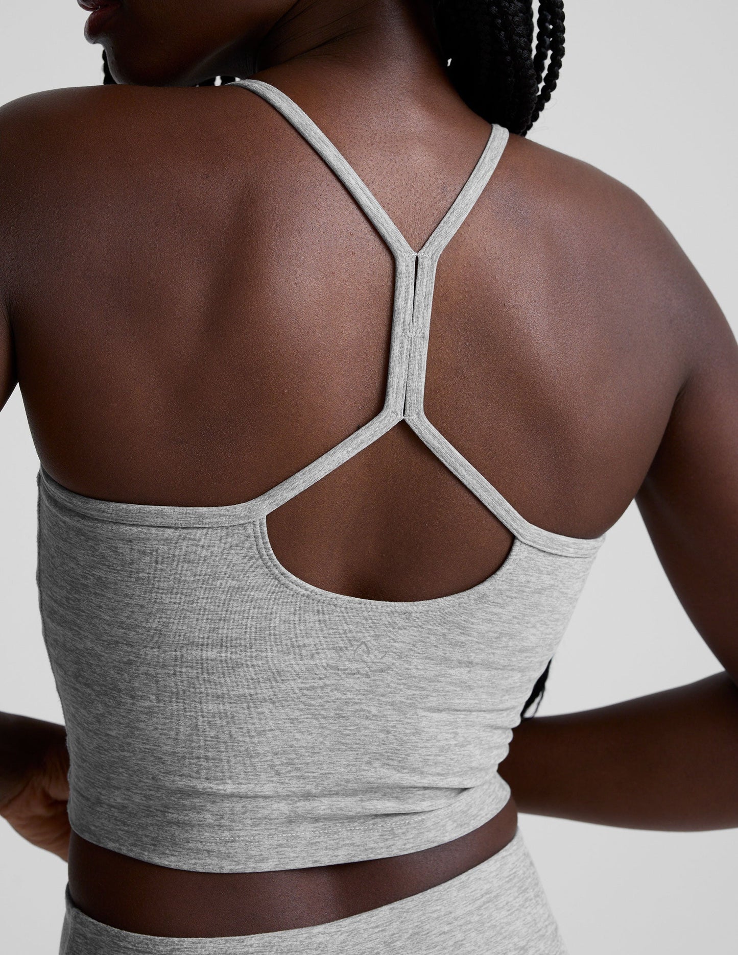 woman is wearing a gray racerback cropped tank and gray leggings against a plain background.