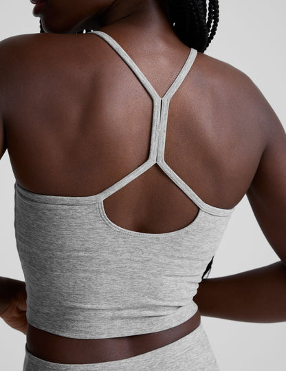 woman is wearing a gray racerback cropped tank and gray leggings against a plain background.