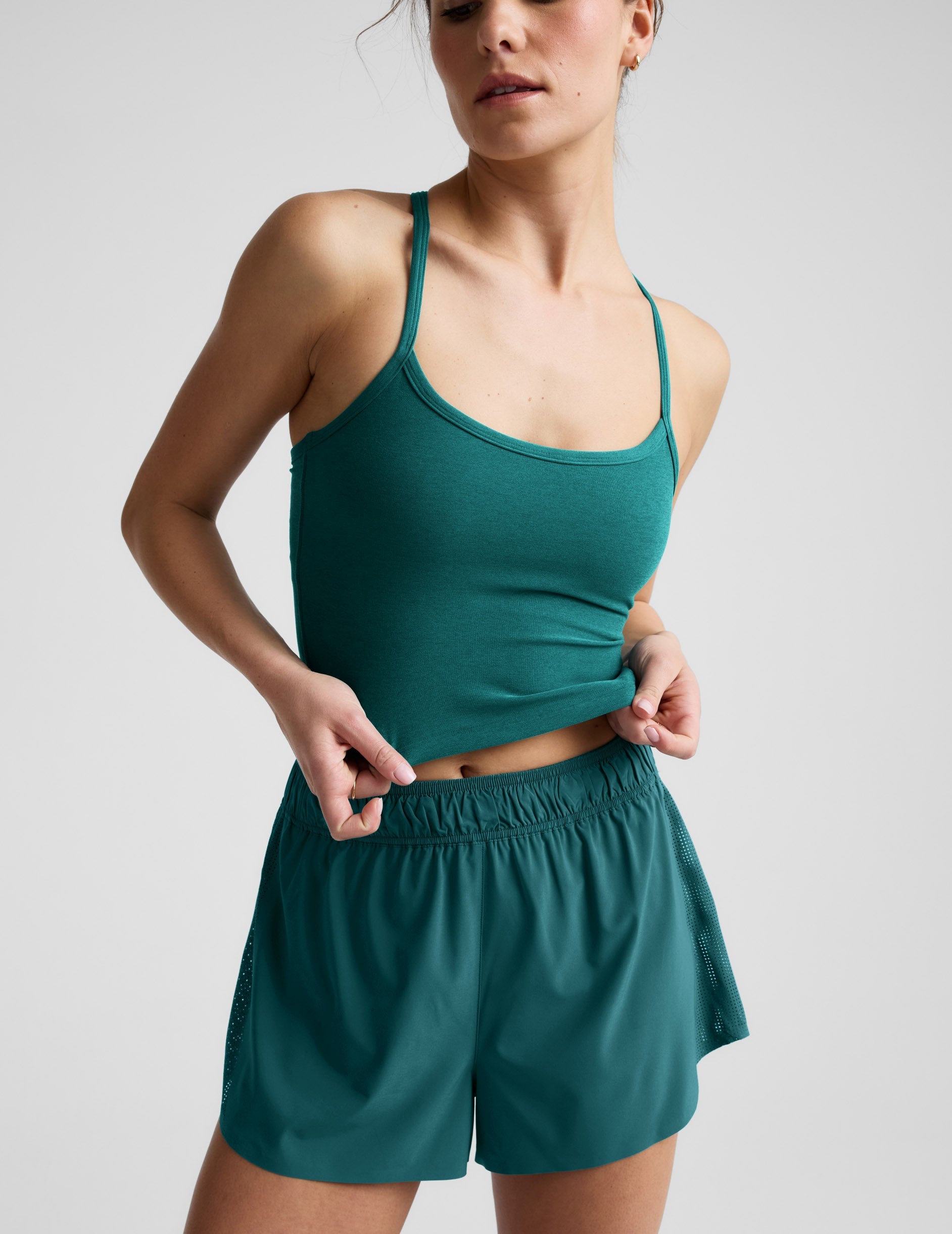 Woman wearing a green cropped tank and shorts against a plain background.