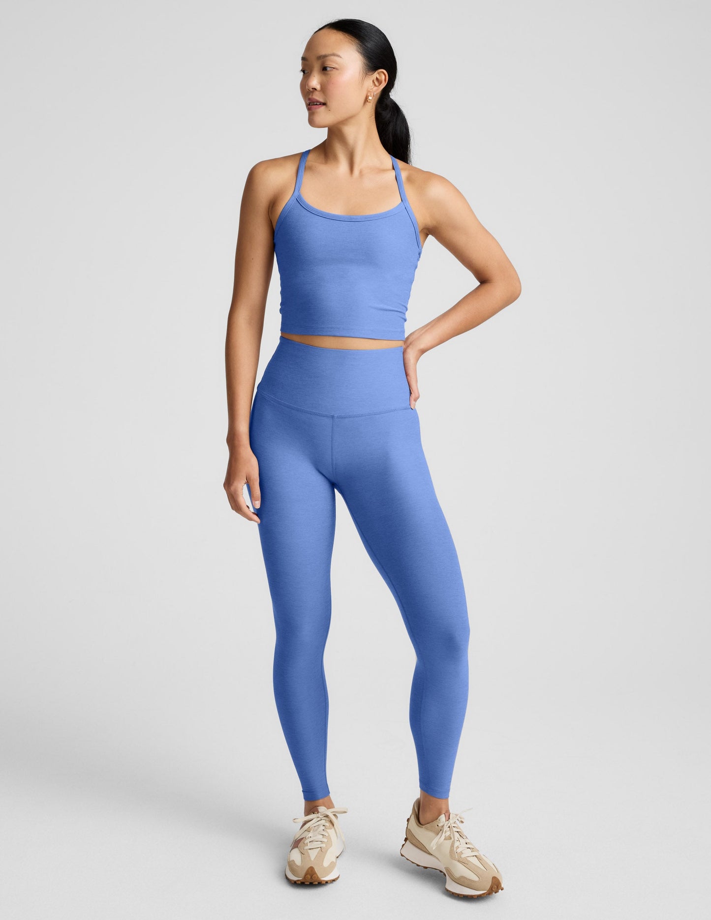 Woman wearing a blue cropped tank and leggings against a light gray background.
