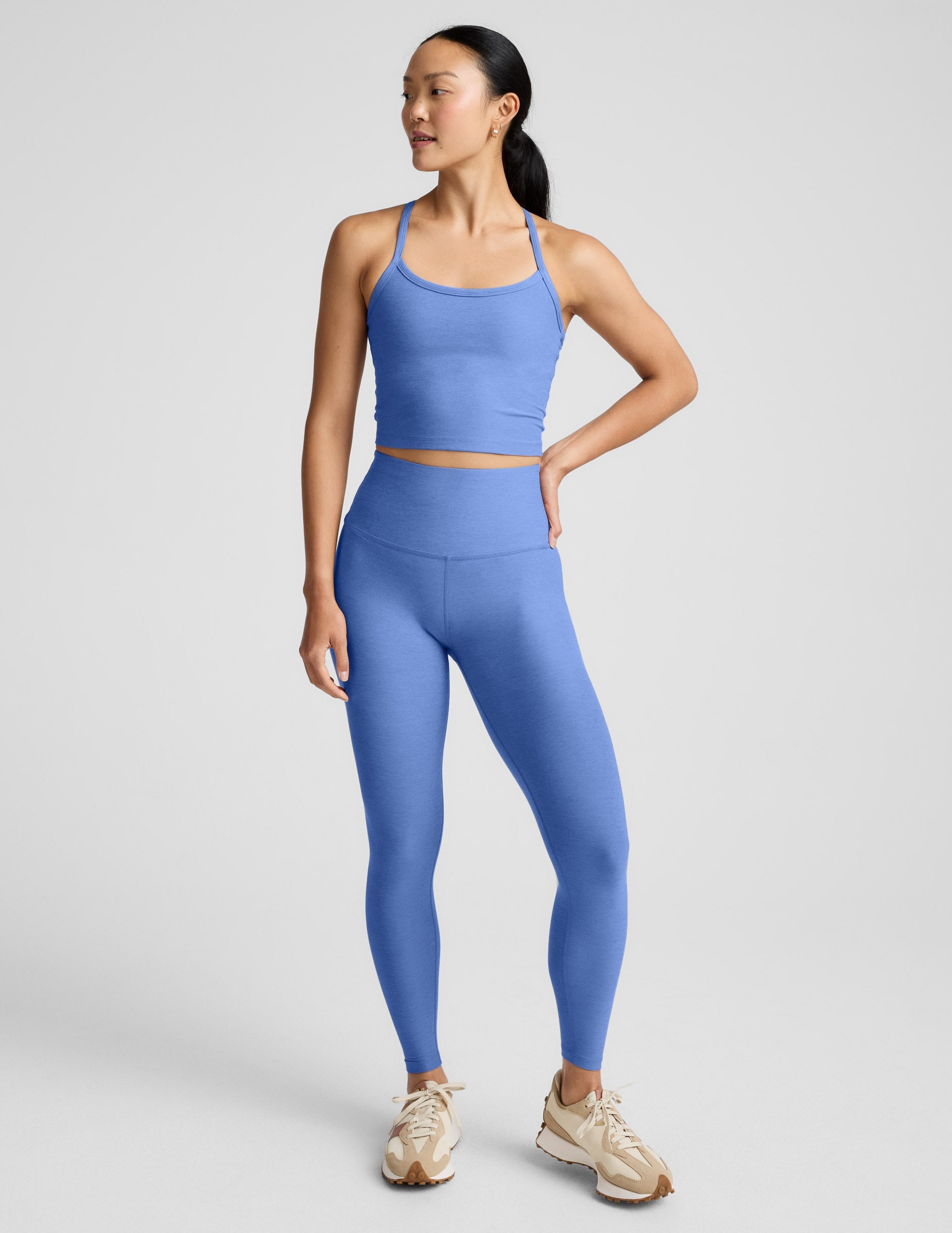 Woman wearing a blue cropped tank and leggings against a light gray background.