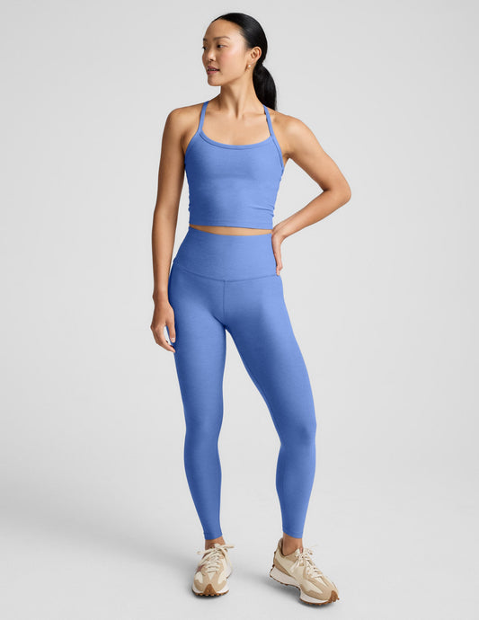 Woman wearing a blue cropped tank and leggings against a light gray background.