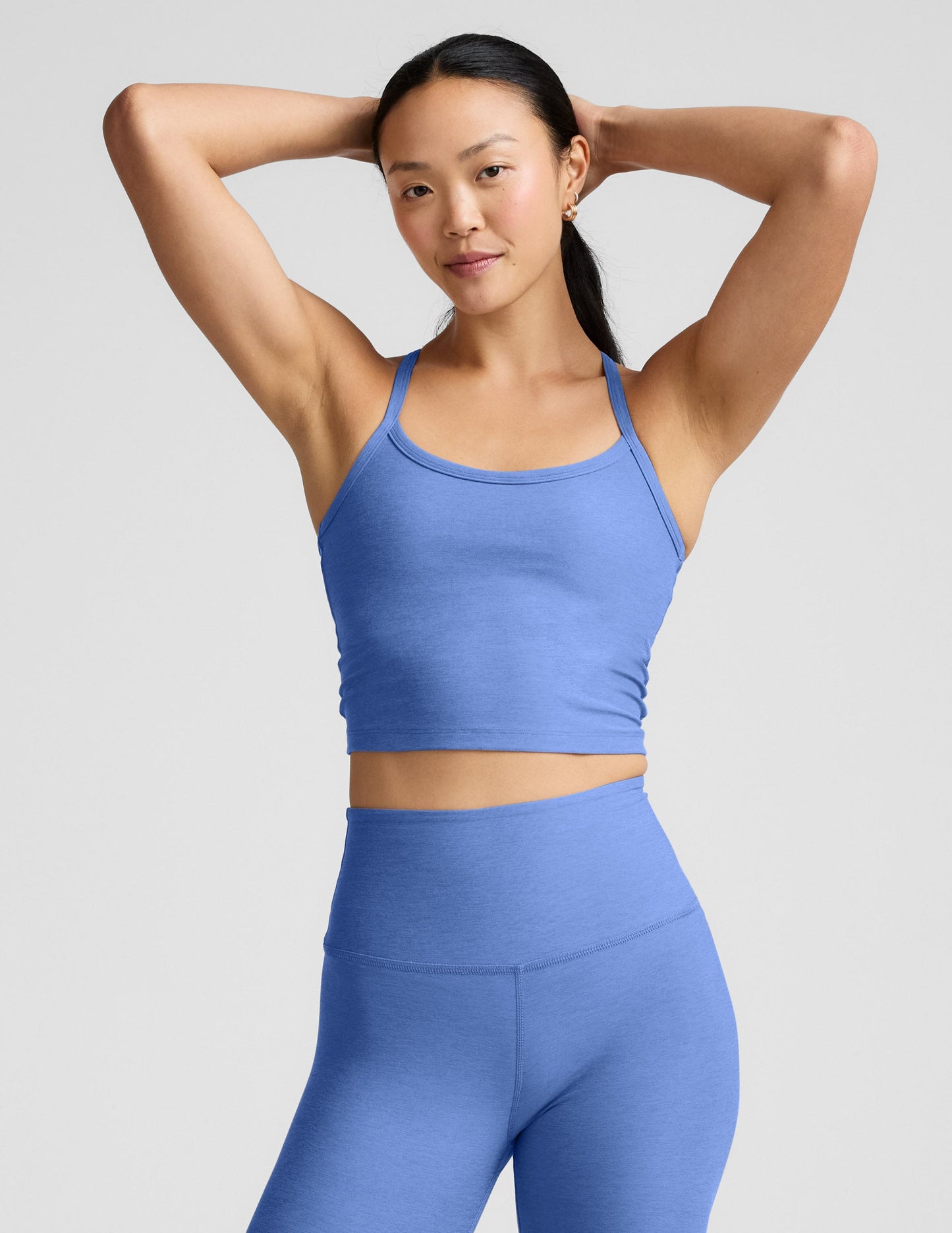 Woman wearing a blue cropped tank and leggings against a light gray background.