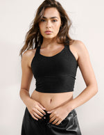 Woman wearing a black cropped tank with twist back details against a plain background.