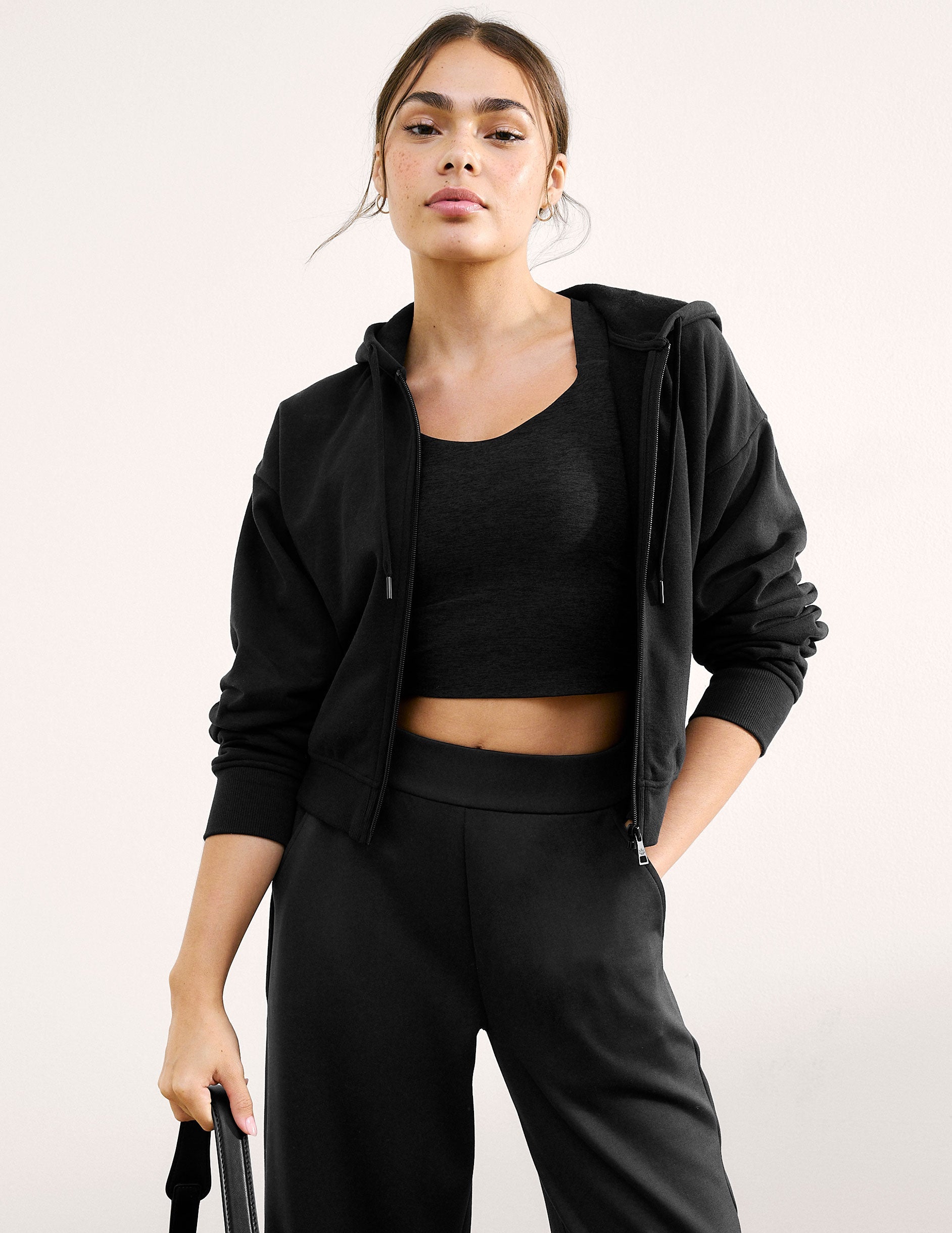 Woman wearing a black cropped tank with twist back details against a plain background.