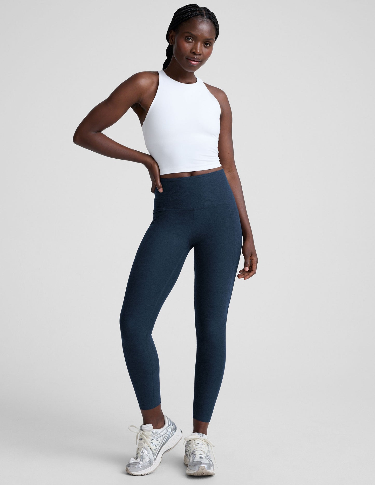 woman wearing a white high-neck racerback cropped tank and navy leggings on a plain background.