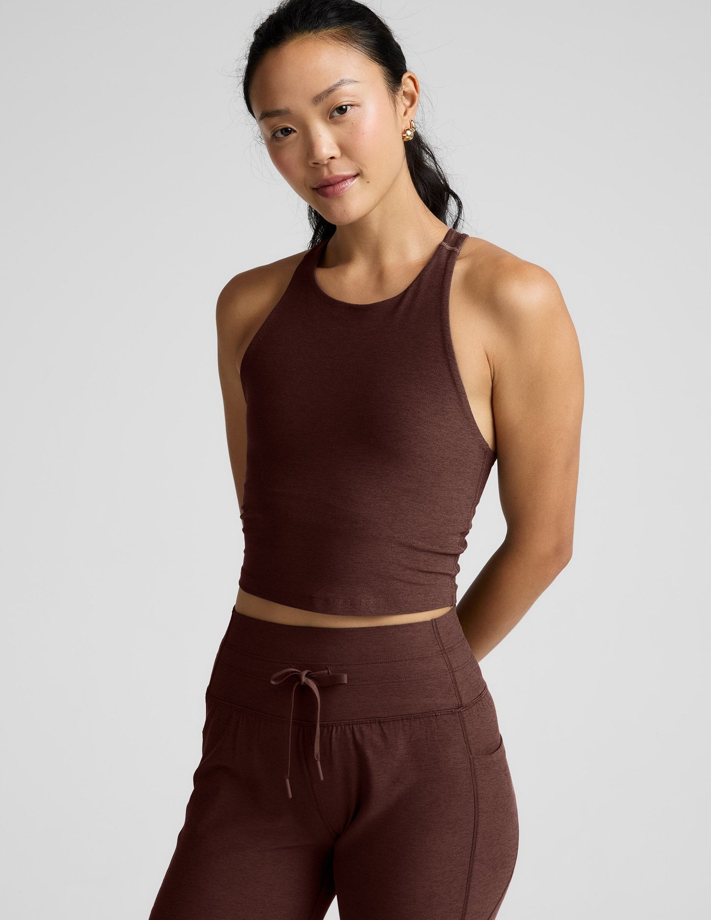 Woman wearing a brown high-neck racerback cropped tank and joggers against a plain background.
