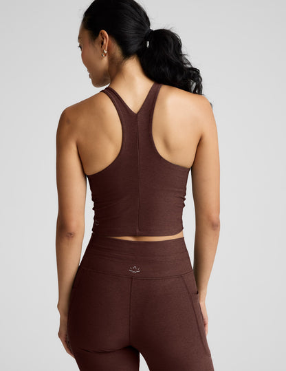 Woman wearing a brown high-neck racerback cropped tank and joggers against a plain background.
