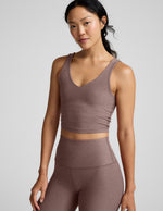 Woman wearing a brown v-neck cropped tank and leggings against a gray background.