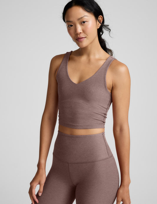 Woman wearing a brown v-neck cropped tank and leggings against a gray background.