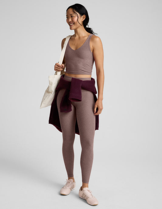 Woman wearing a brown v-neck cropped tank and leggings against a gray background.