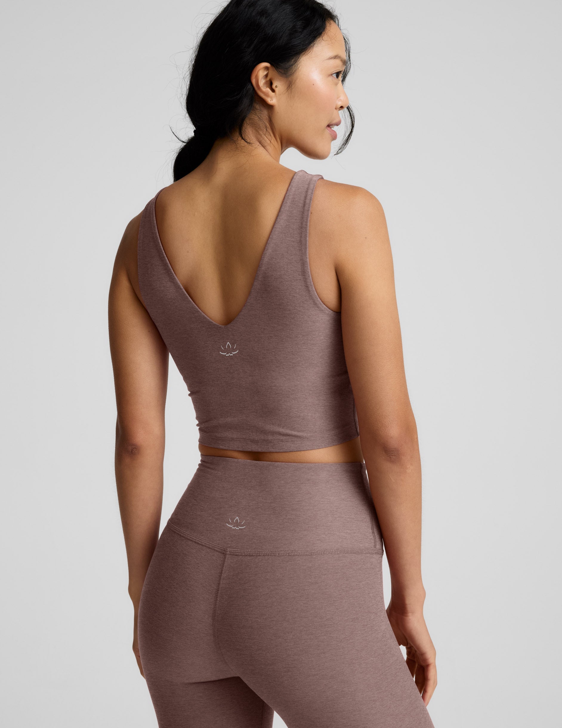 Woman wearing a brown v-neck cropped tank and leggings against a gray background.