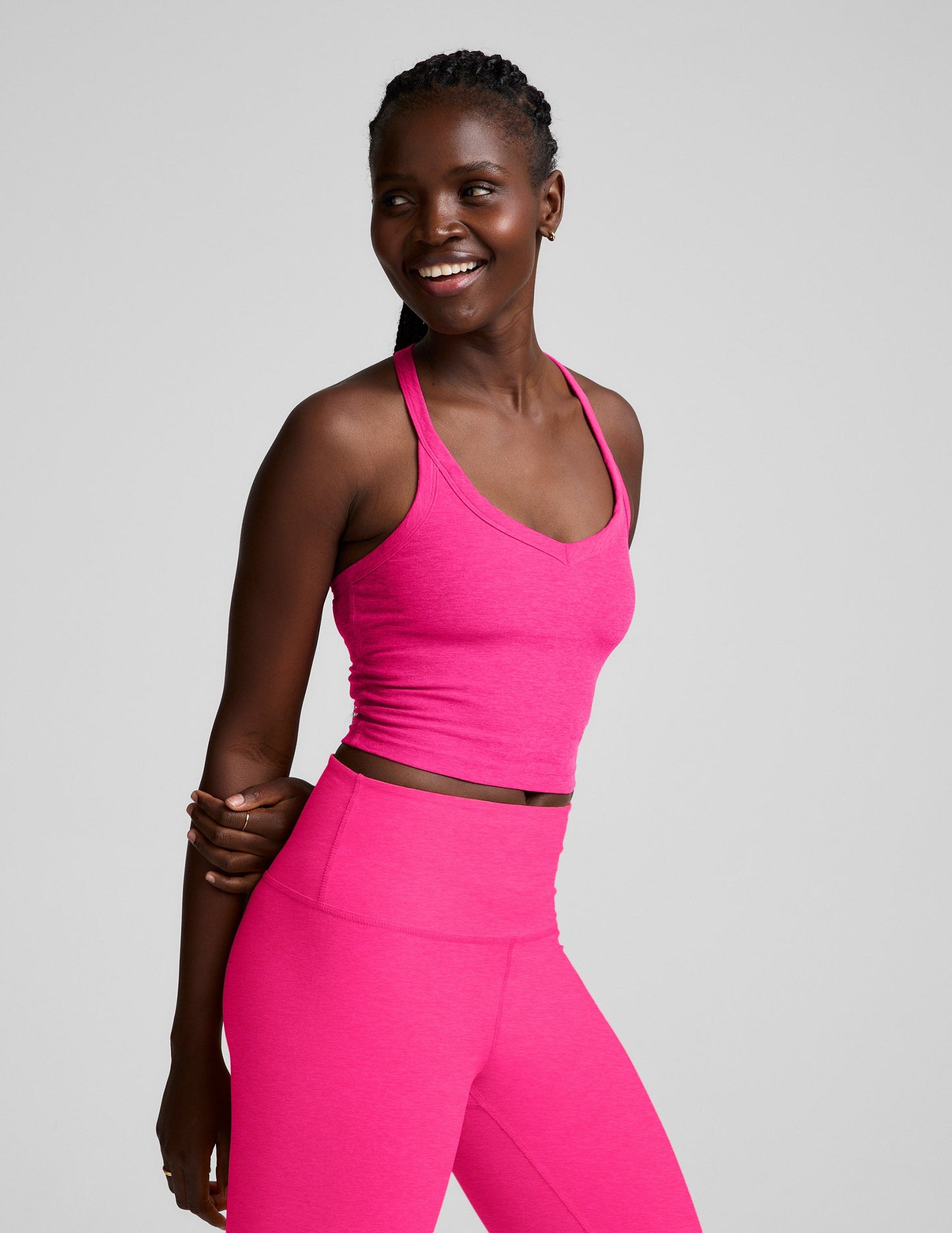 Woman wearing a pink v-neck cropped tank and leggings against a plain background.