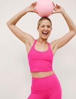Woman wearing a pink v-neck cropped tank and leggings against a plain background.