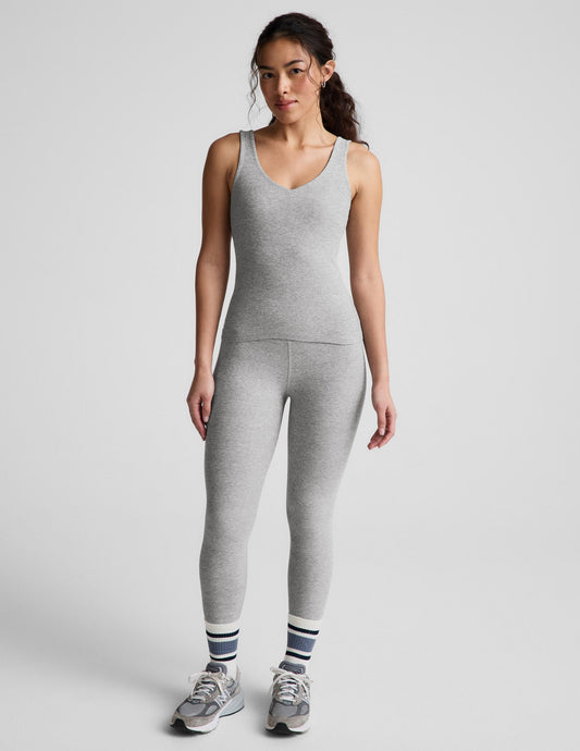 Woman wearing a gray tank top and leggings against a plain background.