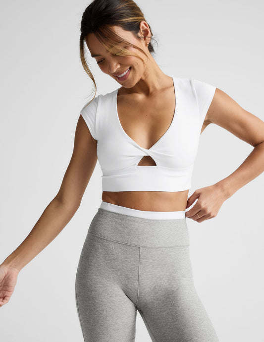 Woman wearing a white crop top and gray pants on a light background.