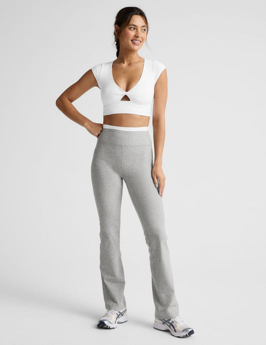 Woman wearing a white crop top and gray pants on a light background.