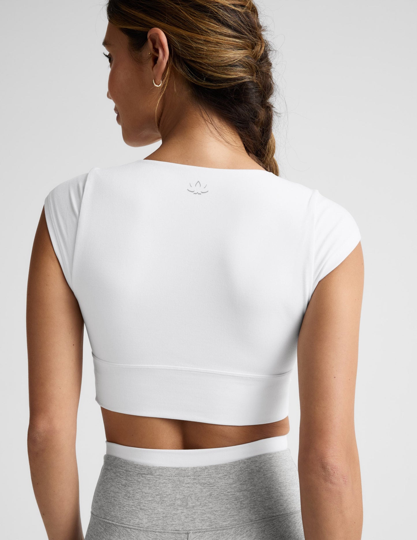 Woman wearing a white crop top and gray pants on a light background.