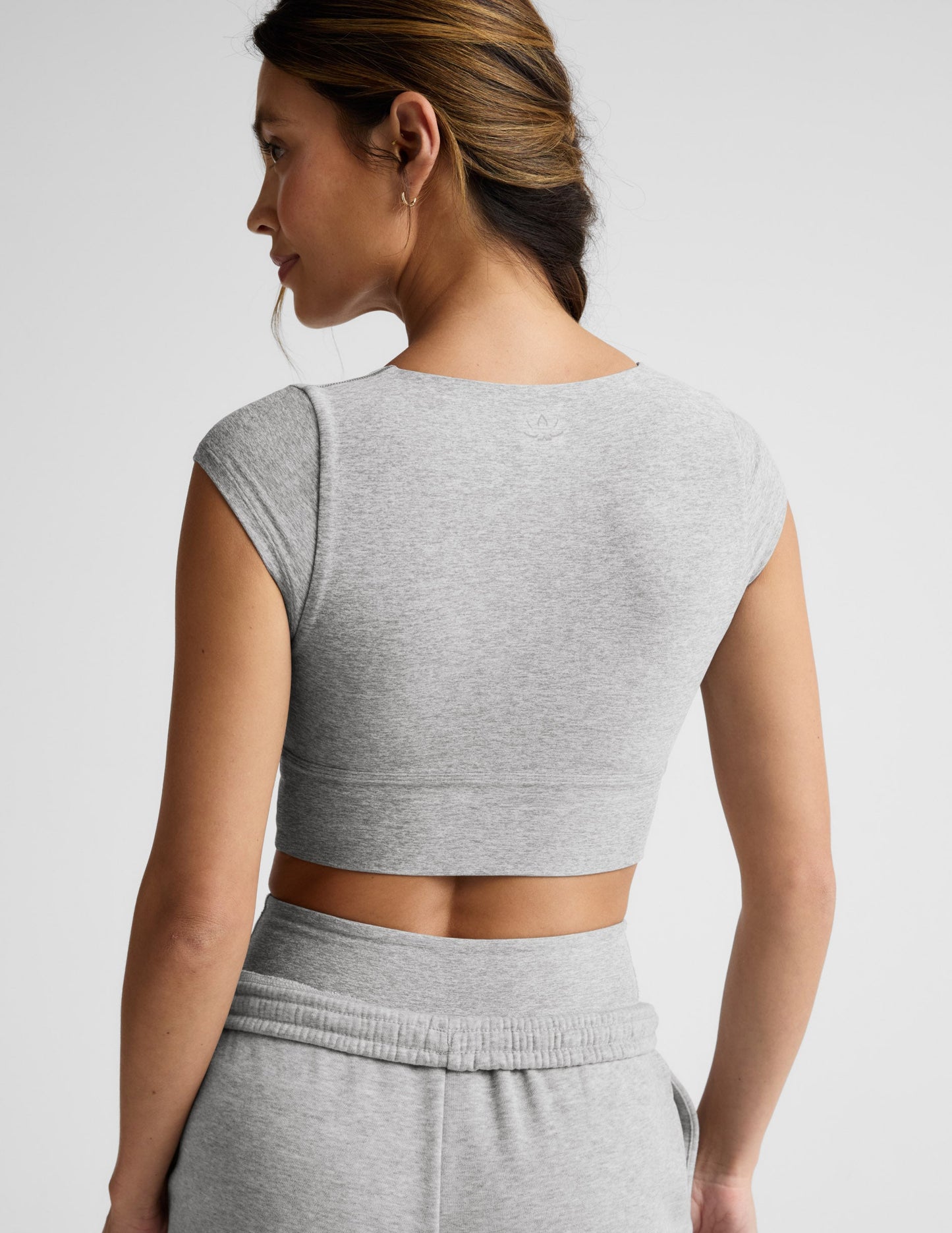 Woman wearing a gray cropped twist tee and sweatpants on a light gray background.