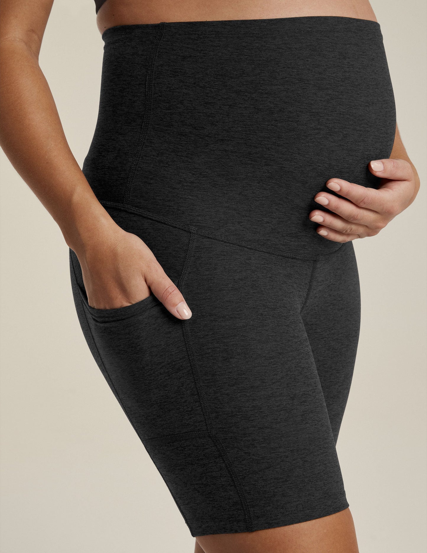 Woman wearing Black marled Spacedye Pockets Forever Maternity Biker Short with hands on bump and in side pocket.