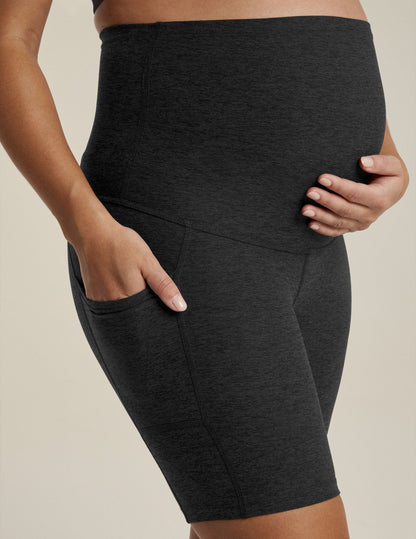 Woman wearing Black marled Spacedye Pockets Forever Maternity Biker Short with hands on bump and in side pocket.