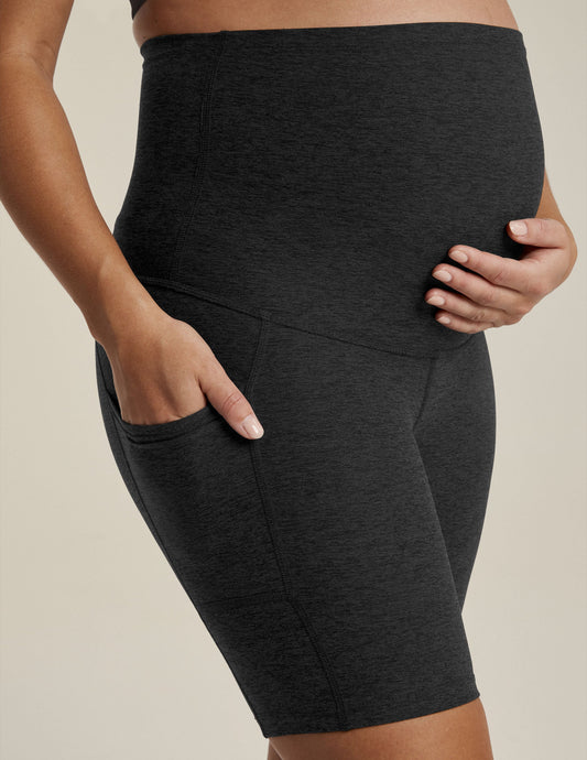 Woman wearing Black marled Spacedye Pockets Forever Maternity Biker Short with hands on bump and in side pocket.