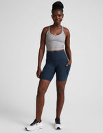 woman wearing a gray tank top and navy blue biker shorts with pockets on a plain background.