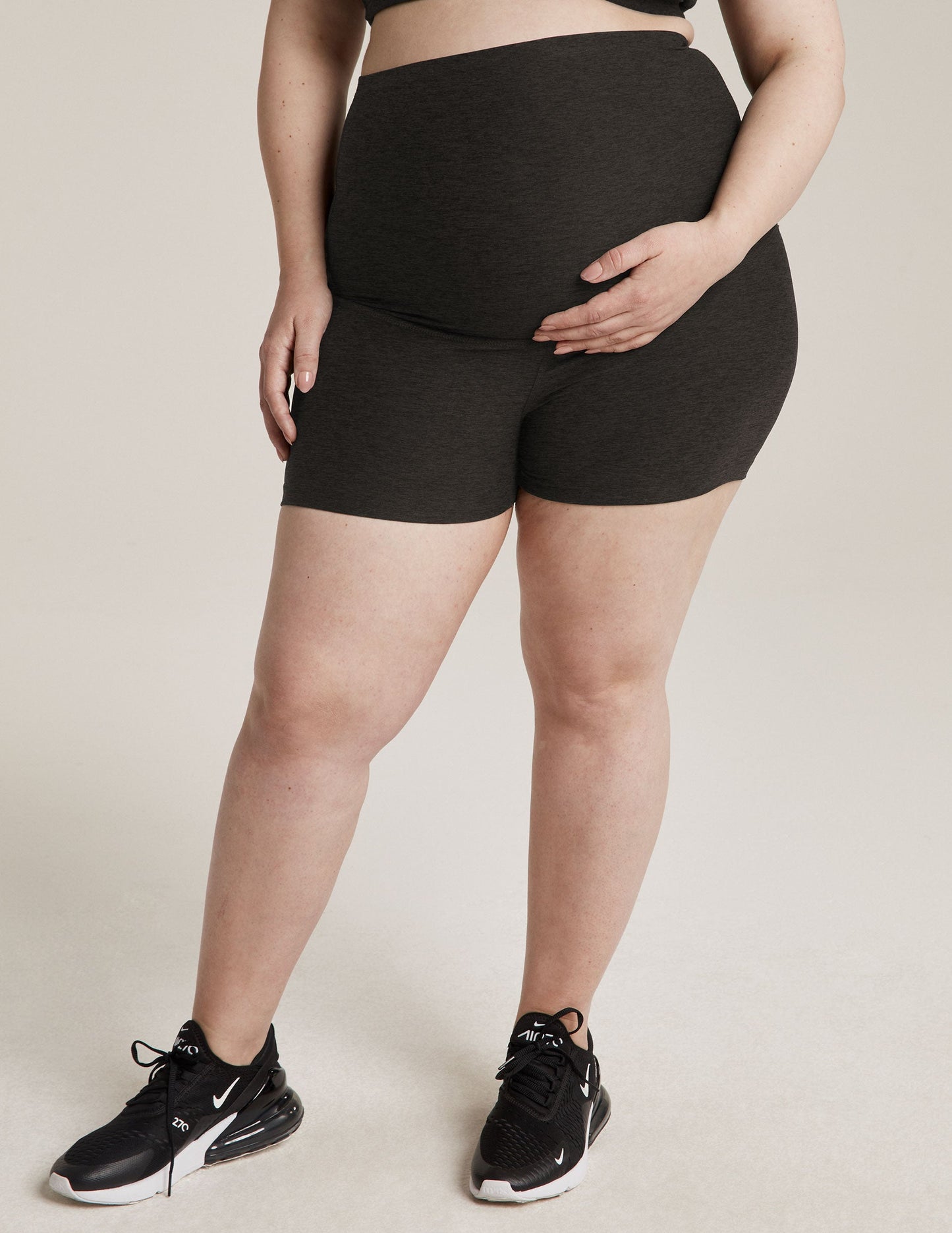 Woman wearing Gray Spacedye All For Run Maternity Short™ over her belly, paired with black sneakers.