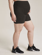 Woman wearing Gray Spacedye All For Run Maternity Short™ over her bump paired with black sneakers in a side profile.