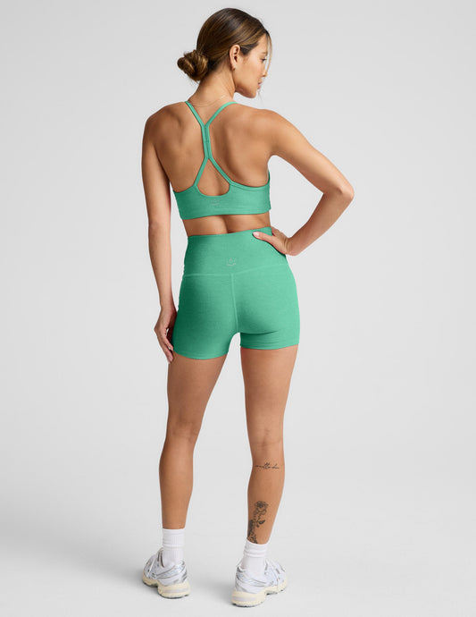 Back view of a woman wearing green Spacedye Keep Pace 3" Shorts with a high waistband and matching sports bra.