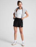 A woman wears the black Spacedye Points Crossover Skirt, a mini A-line skort featuring a front side overlap slit.