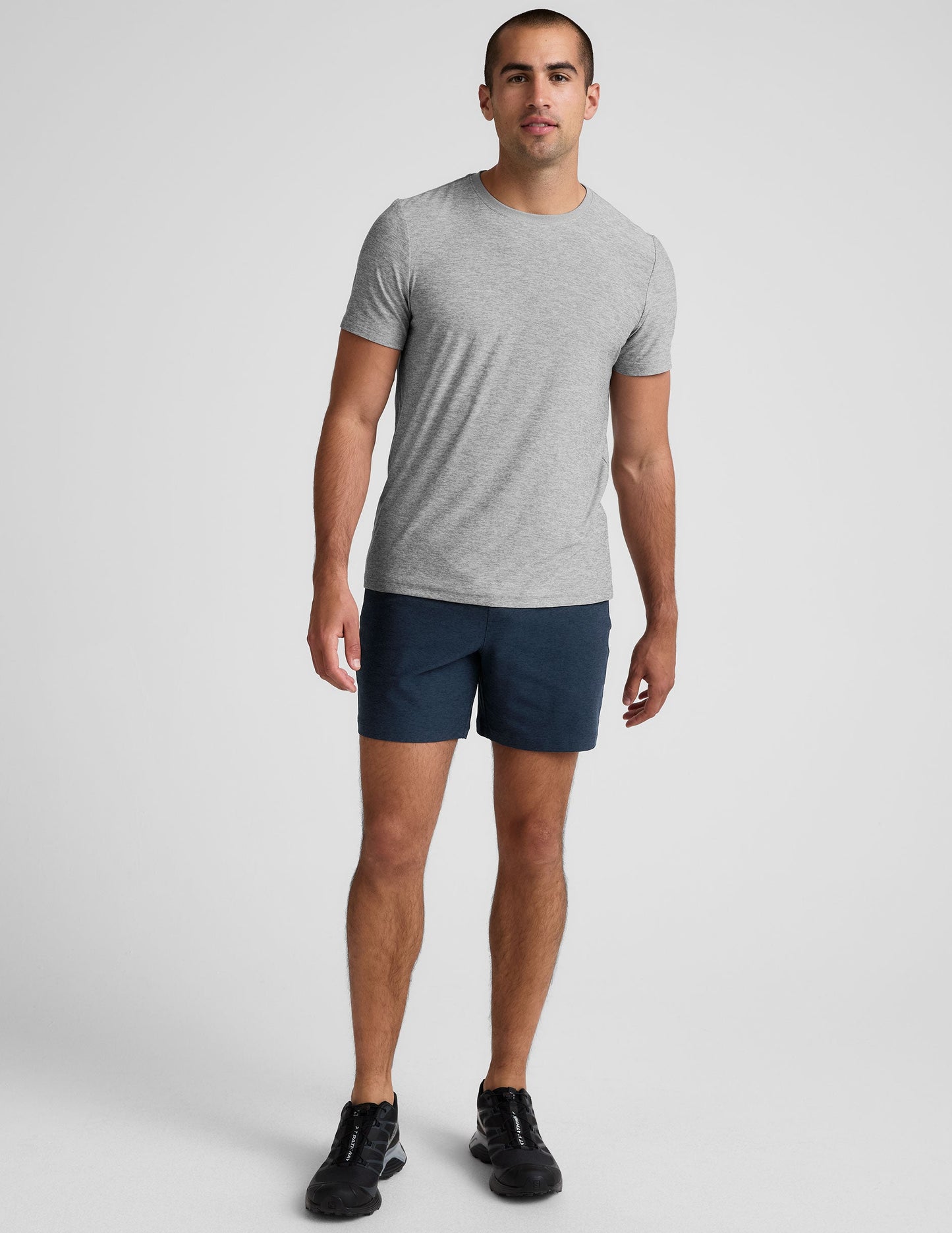 Man wears navy Spacedye Unlimited Men's Shorts with a 7" inseam, paired with a grey t-shirt and black sneakers.
