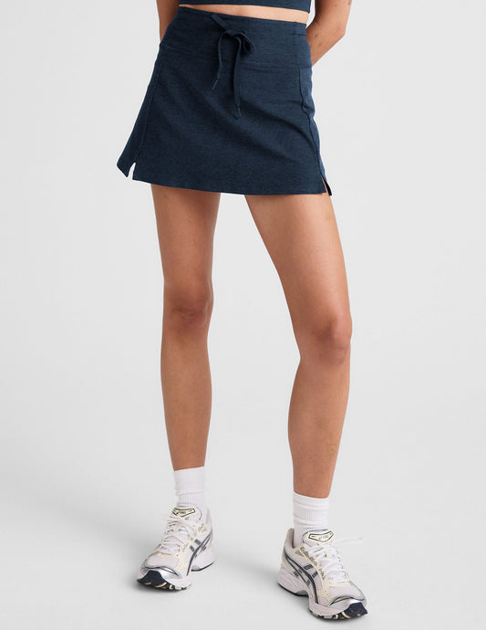 Navy Spacedye Go Pocket Skirt with high waistband, drawstring, and side slits on a model with white sneakers.