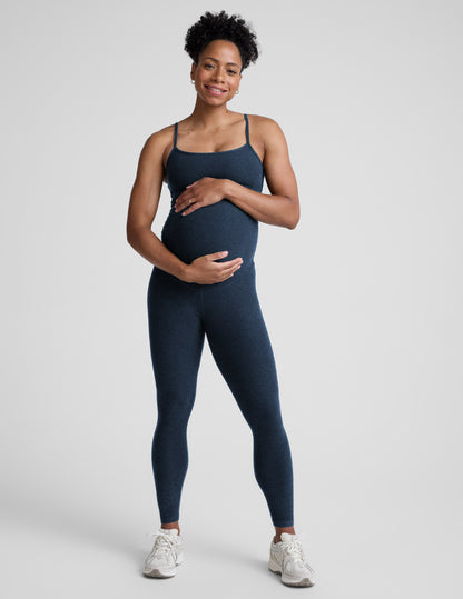 Pregnant woman wearing a navy blue jumpsuit on a light gray background.
