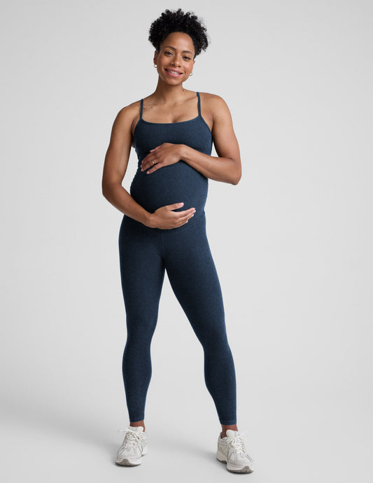 Pregnant woman wearing a navy blue jumpsuit on a light gray background.
