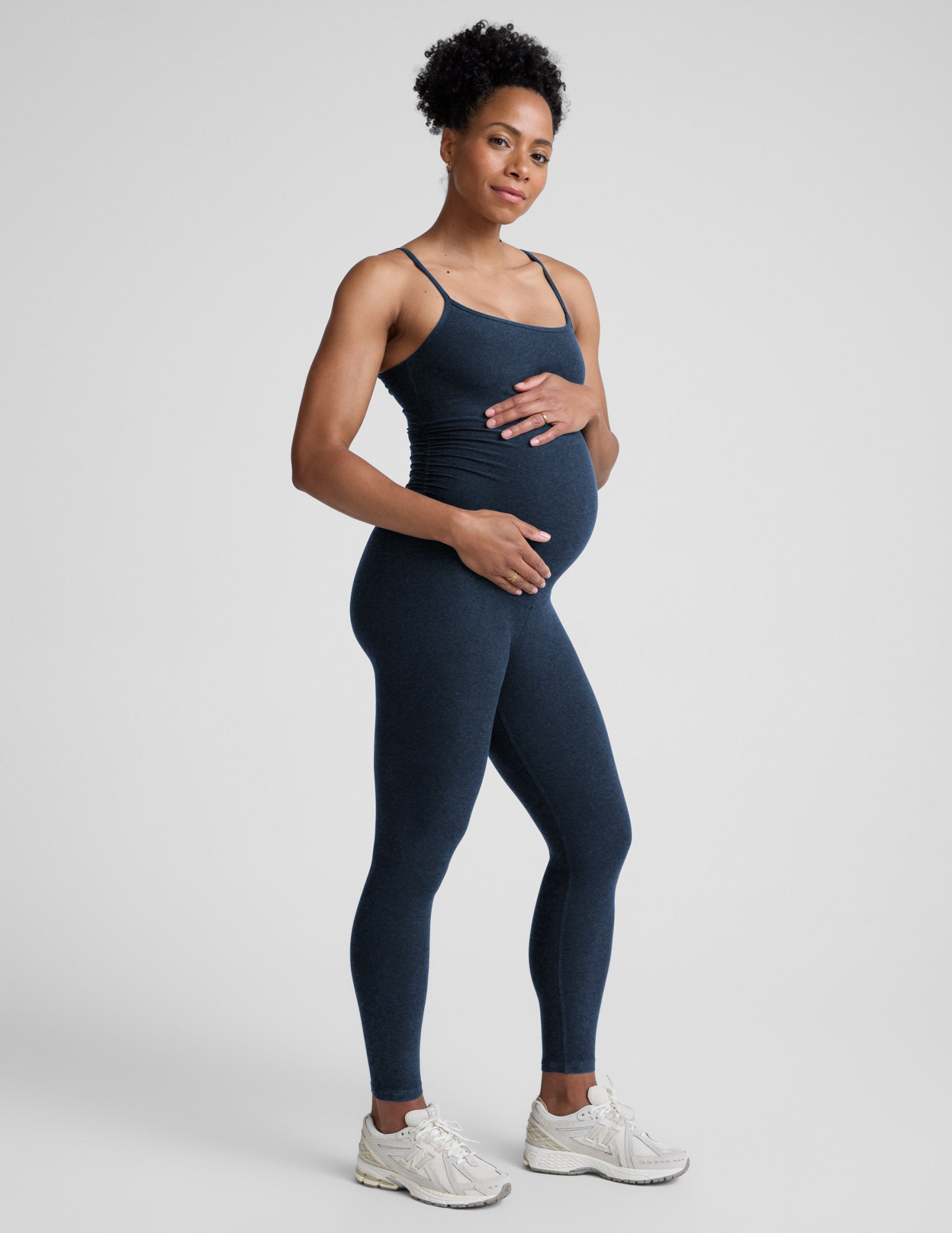 Pregnant woman wearing a navy blue jumpsuit on a light gray background.