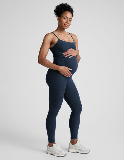 Pregnant woman wearing a navy blue jumpsuit on a light gray background.